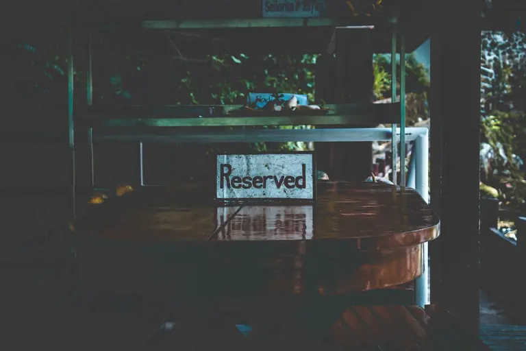 A dimly lit table with a reserved sign, set in an outdoor environment creating a moody atmosphere.