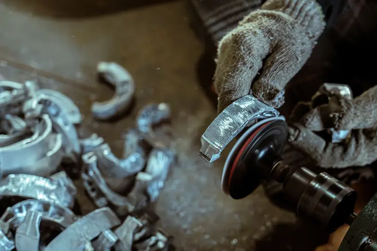 Close-up of hands polishing metal brake pads with a grinder in a workshop.