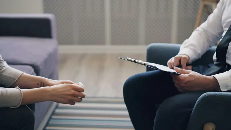 A person holding a tissue facing another person with a clipboard in a room