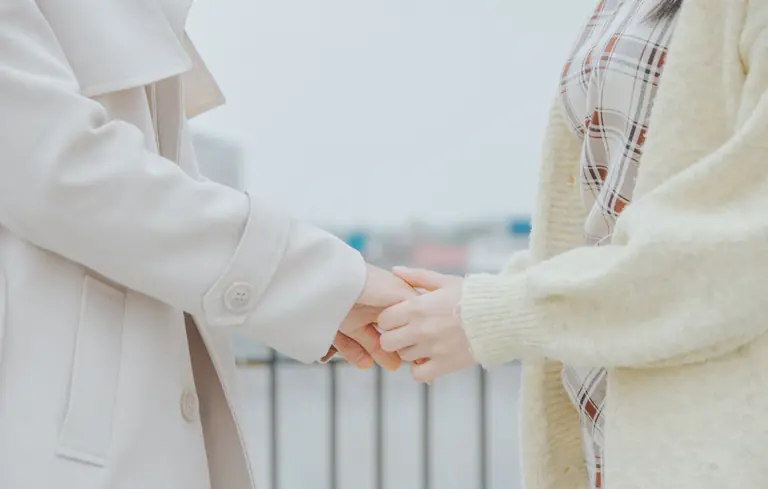 A close-up of two people holding hands while wearing warm coats outdoors.