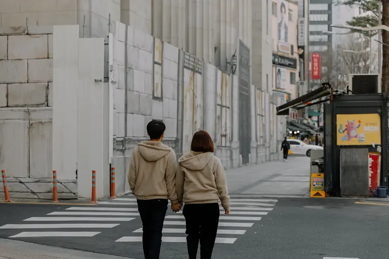 A couple walks hand in hand on a city street crosswalk, urban lifestyle.