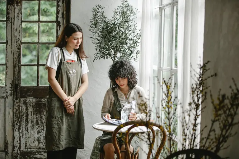 Young waitress waiting for focused female client turning pages of menu while making order in cafe