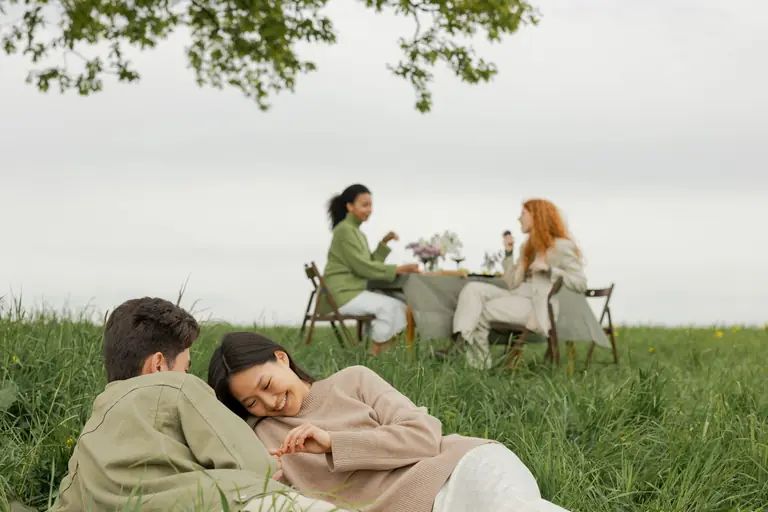 A couple and friends enjoy a serene picnic on a grassy field, creating a warm and friendly atmosphere.