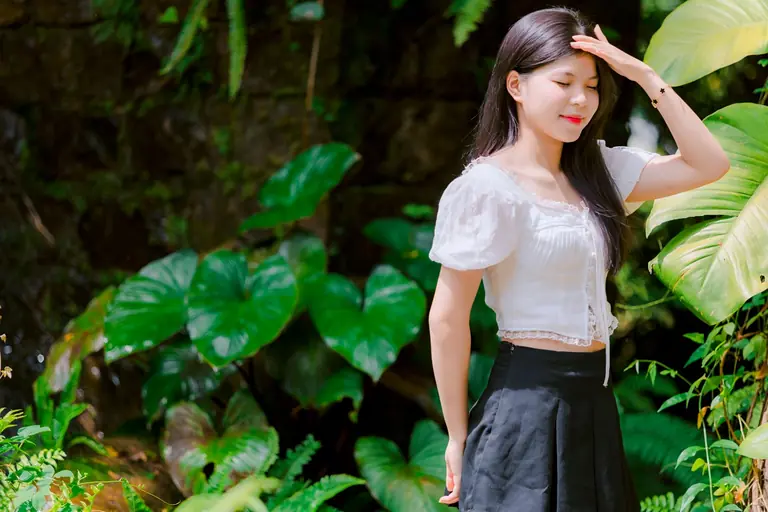 Smiling young woman enjoying a sunny day surrounded by vibrant green leaves.